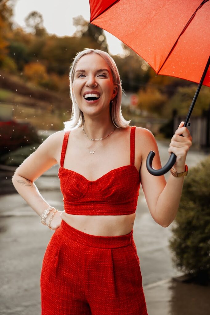 Katrina Owens, a PR expert who knows how boutique PR agency settings function, stands in a two-piece red outfit and a red umbrella outdoors