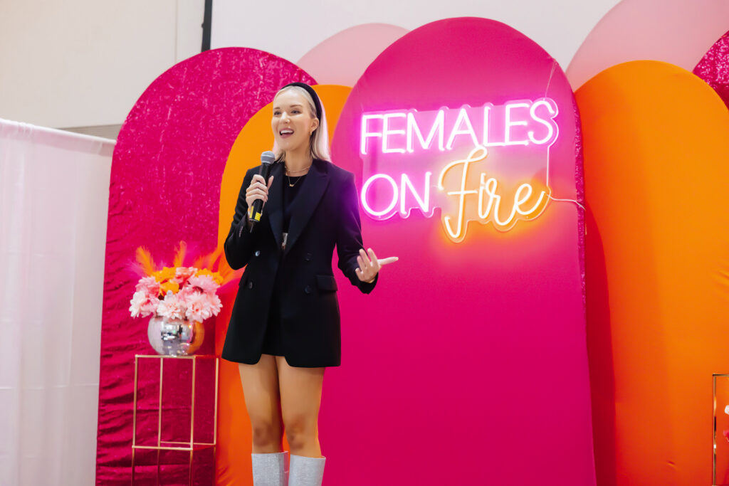 Personal Brand Coach Katrina Owens shares tips for building confidence and executive presence while on stage wearing a long black blazer and a black headband