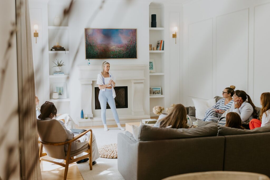 Katrina Owens wears a light blue activewear two-piece set while smiling and holding a notebook in a neutral living room full of local entrepreneurs building personal brands