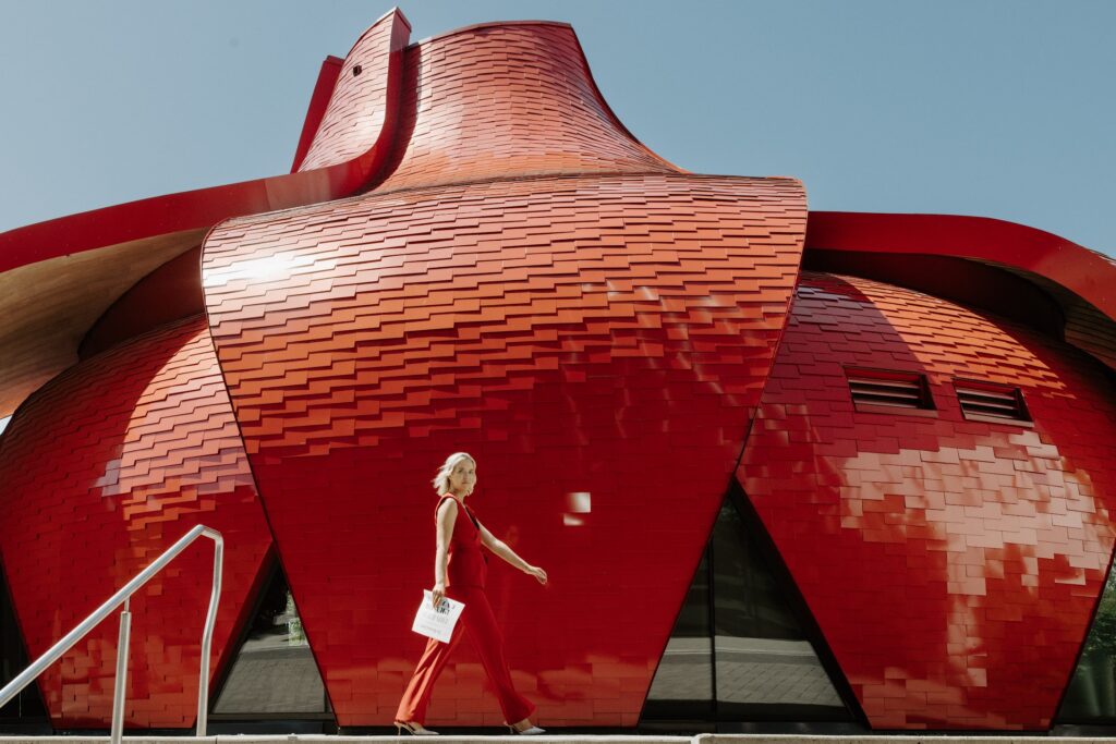 PR for interior designers expert Katrina Owens strolls across a red building wearing a red sleeveless 2-piece suit