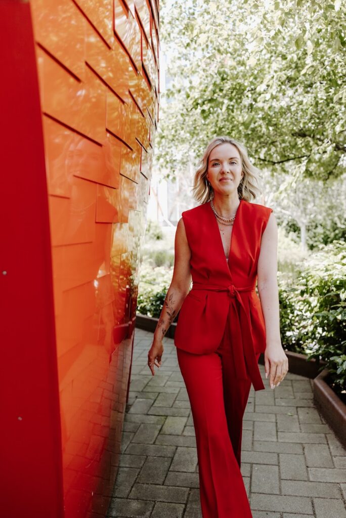 Katrina Owens, who teaches PR for interior designers and entrepreneurs, strolls outside on a stone walkway in a sleeveless red 2-piece suit