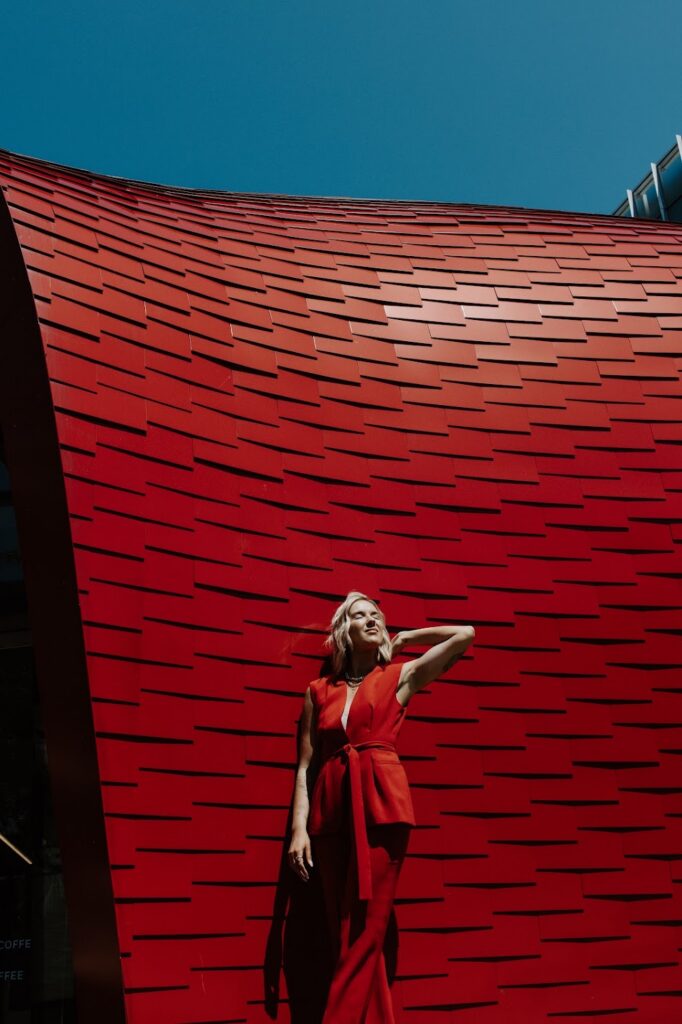 PR and personal brand coach Katrina Owens wears a 2-piece sleeveless red suit in front of a red building with contrast from the light and shadows