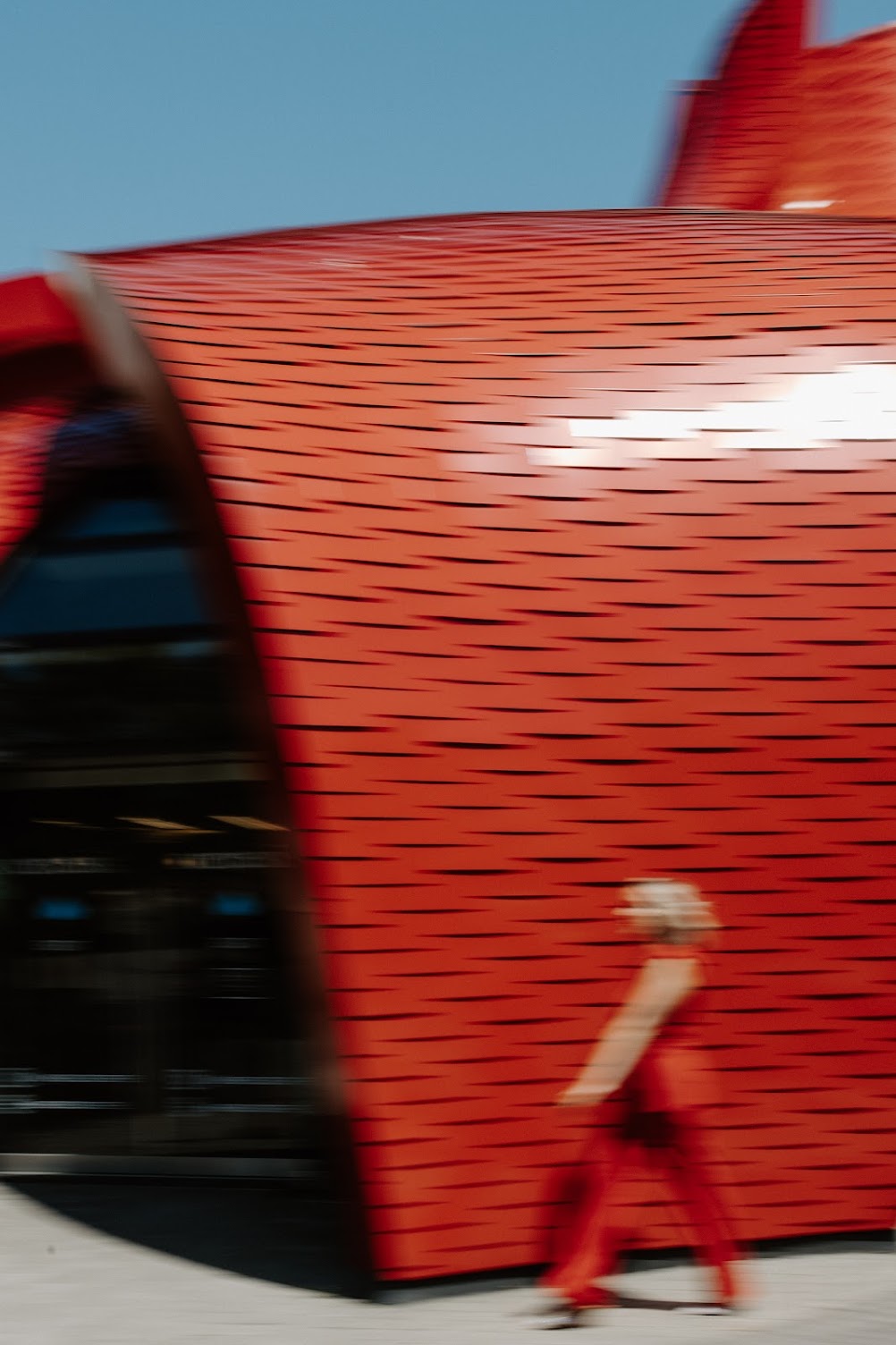 Blurry photo of keynote speaker and PR expert Katrina Owens strolling outside past a red building wearing a red outfit