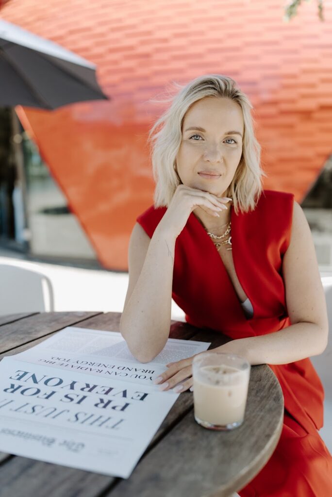 Public relations for interior designers expert Katrina Owens sits at a round wooden table with iced coffee in a cup reading the newspaper