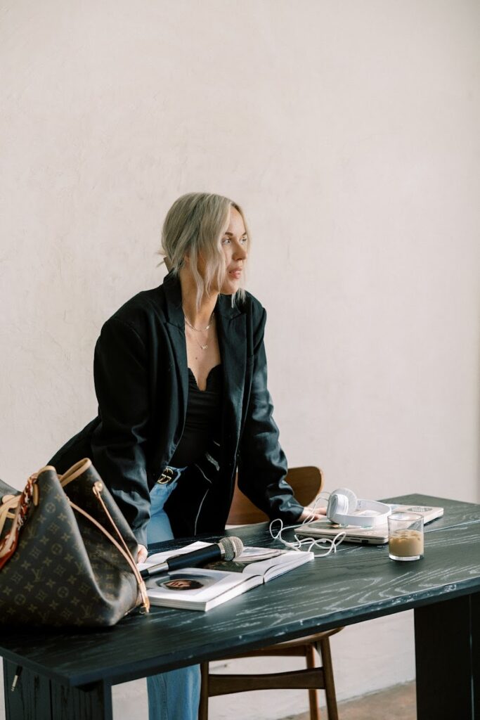 personal branding speaker and coach Katrina Owens wears a black blazer and jeans leaning over a desk in her personal brand expert office