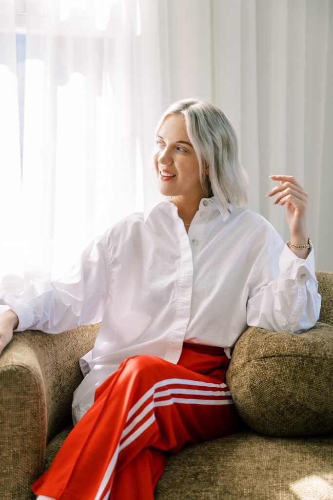 Katrina Owens, an expert in how to improve visibility using PR and personal branding, sits in a chair in a white button-up shirt and red pants