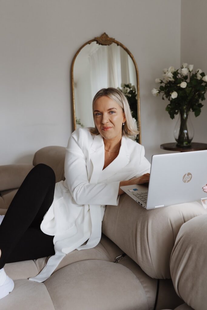 Personal Brand Coach Katrina Owens sits on a couch in a white room on her laptop teaching her clients about landing successful brand partnerships