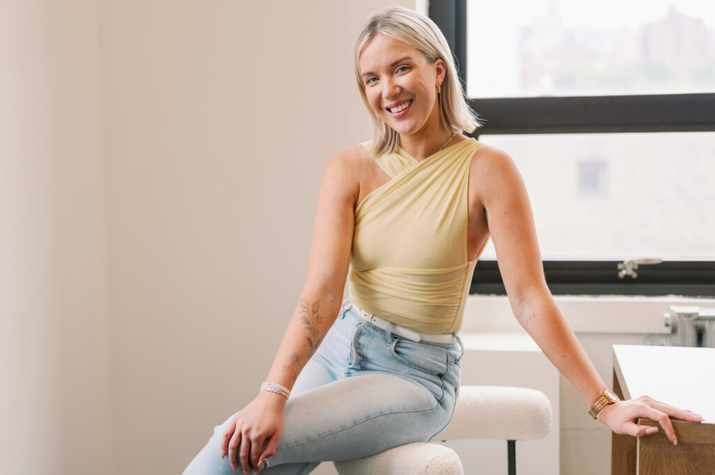 personal brand coach Katrina Owens sits on the shoulder of a white chair wearing jeans and a butter yellow top
