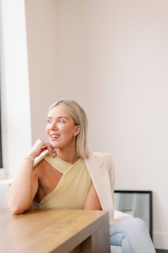 Podcaster Katrina Owens shares her tips for starting a podcast and monetizing a podcast while sitting in a butter yellow top and white blazer in a naturally lit white room