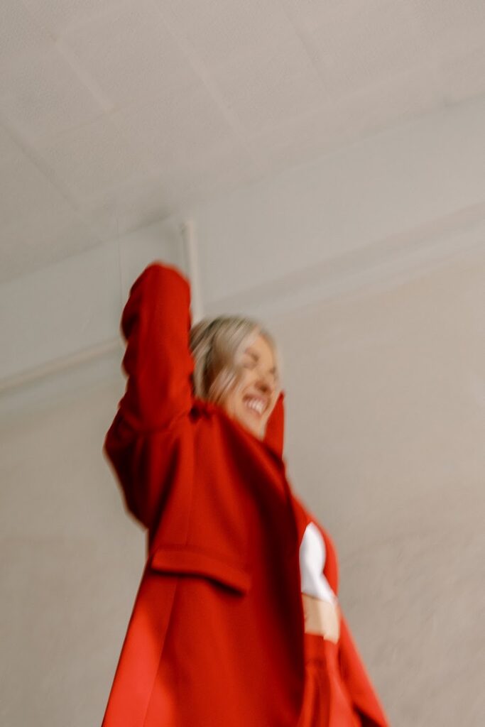 A blurry photo of Personal Branding coach Katrina Owens in a red blazer, white top, and red pants with her hands in the air as she's smiling