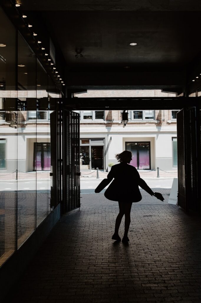 The silhouette of Katrina Owens photographed walking on a cobblestone walkway towards a door  opening in an urban area