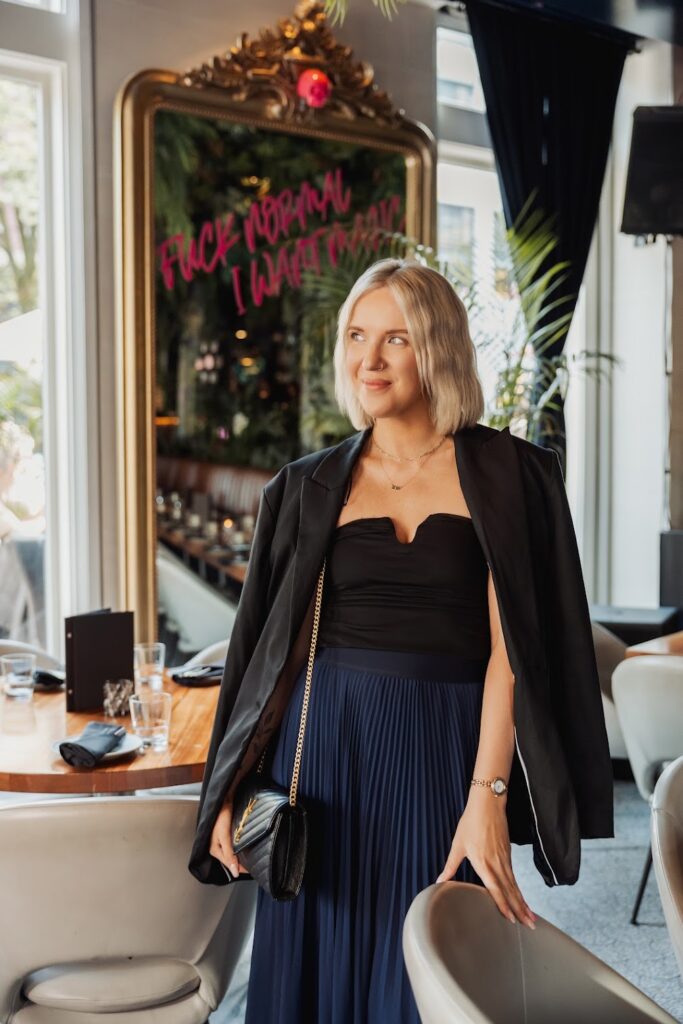 Personal brand strategist Katrina Owens standing in a navy blue skirt and black top with black blazer in front of a mirror