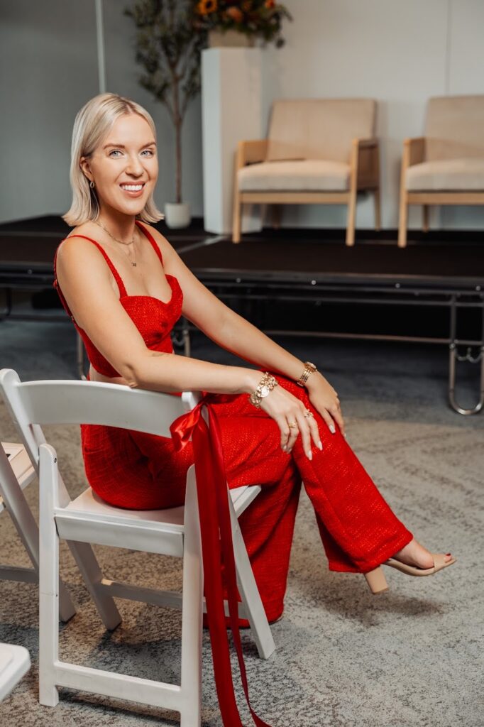 Katrina Owens sits in a white chair at an event where she's speaking in front of an audience on building a personal brand and more